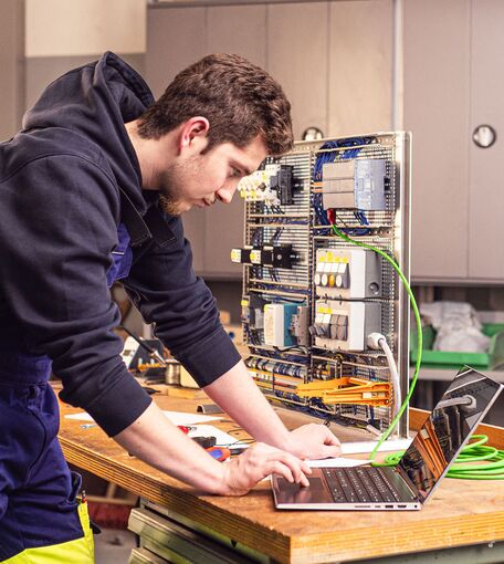 Ein junger Mann arbeitet an einem Laptop an einem über Kabel verbundenen elektronischen System.