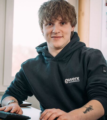 Ein junger Mann mit dem Logo ewerk Sachsenwald sitzt an einem Computer.