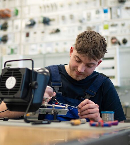 Ein junger Mann arbeitet in einer Werkstatt konzentriert an einem elektronischen System.