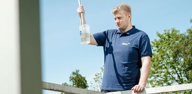 Ein junger Mann entnimmt eine Wasserprobe und betrachtet diese im Sonnenlicht.