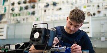 Ein junger Mann arbeitet in einer Werkstatt konzentriert an einem elektronischen System.