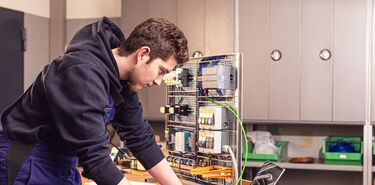 Ein junger Mann arbeitet an einem Laptop an einem über Kabel verbundenen elektronischen System.