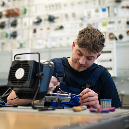 Ein junger Mann arbeitet in einer Werkstatt konzentriert an einem elektronischen System.