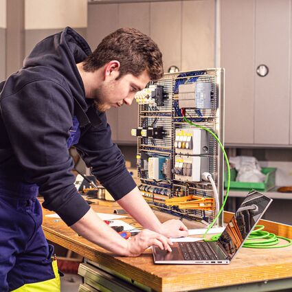 Ein junger Mann arbeitet an einem Laptop an einem über Kabel verbundenen elektronischen System.